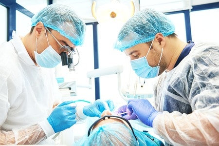 two male dentist in uniform perform dental implantation operation on a patient at dentistry office