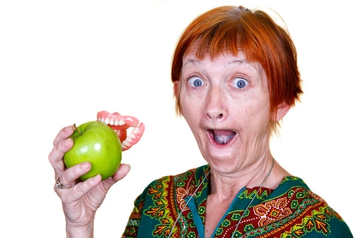 Elderly lady losing her teeth on a bite of an apple